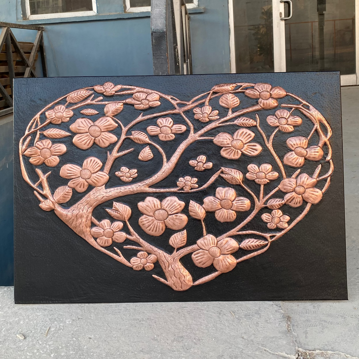 Decorative metal wall art with floral design on a black background, outdoors.