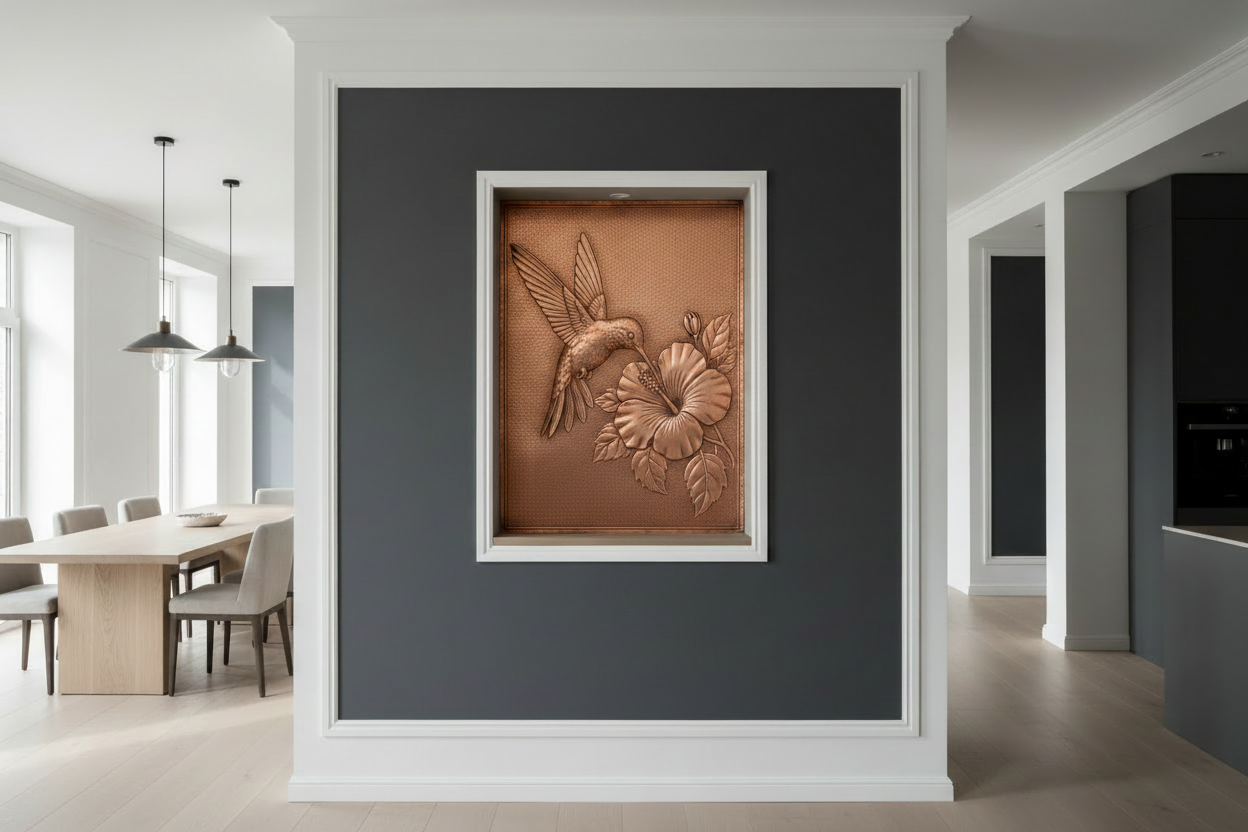 Hand-hammered copper panel fitted inside deep recessed architectural niche with dark charcoal walls — hummingbird in mid-hover with wings fully spread reaching toward large open hibiscus flower in repoussé relief, intricate feather and petal detail, warm rose-gold copper glowing dramatically inside dark niche opening