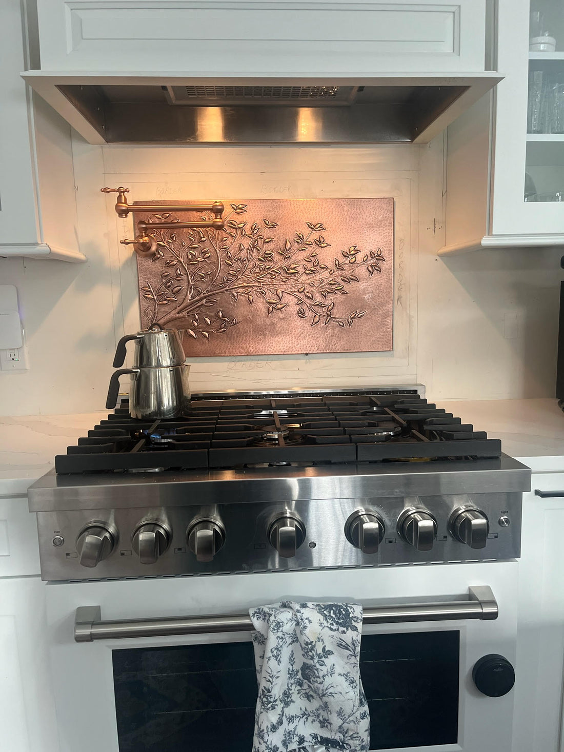 Copper kitchen backsplash installed behind a stove — heat-resistant, hand-hammered copper panel
