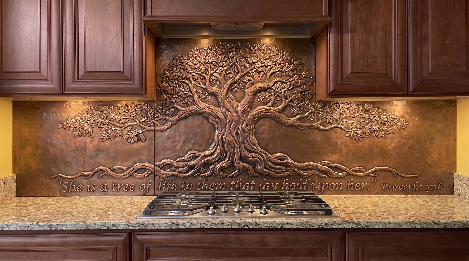Handcrafted Ancient Tree of Wisdom copper kitchen backsplash inspired by Proverbs 3:18, featuring a massive old Tree of Life with a thick trunk, spreading branches, and exposed roots in raised metal relief across the stove and under-cabinet backsplash areas.