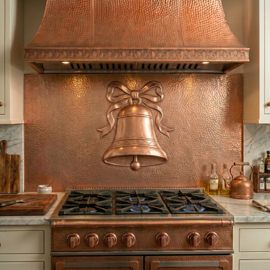 Handcrafted copper stove backsplash featuring a classic Christmas bell and decorative ribbon in repoussé copper. Order a single backsplash panel behind the stove or a complete custom copper kitchen backsplash with matching side panels beneath surrounding cabinets. Available in custom sizes, finishes, and installation options.