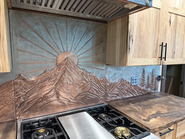 Custom copper kitchen backsplash panels with mountain design under copper range hood