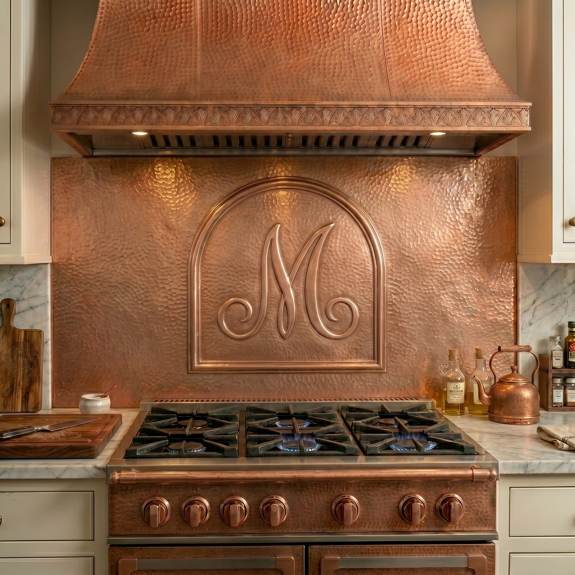 Handcrafted copper kitchen backsplash featuring a personalized monogram framed within an elegant architectural arch. Custom sizes, letters, and finishes available for stove backsplashes and complete kitchen installations.