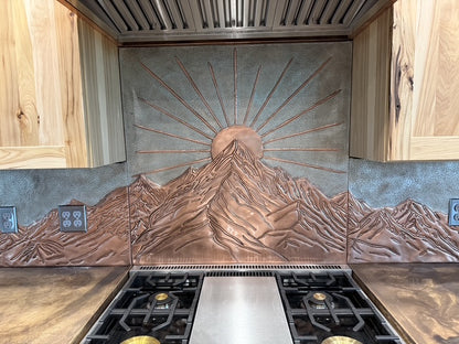Full-wall copper kitchen backsplash set with raised mountain landscape behind range