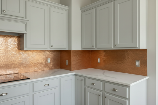 Hand-hammered copper backsplash with side return panel wrapping kitchen corner — wide main panel on back wall and narrow matching return panel on perpendicular side wall, warm rose-gold copper with thin raised border, clean L-shaped installation, white shaker cabinet kitchen
