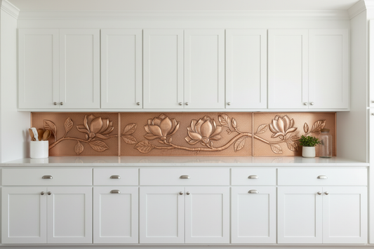 Three copper panels spanning full long counter wall in bright white Shaker kitchen — continuous magnolia branch with large blooms, buds and broad leaves in repoussé relief flowing across all three panels, warm natural copper tone matching magnolia reference, fine stipple background, realistic hairline seams, white shaker upper cabinets, white quartz countertop
