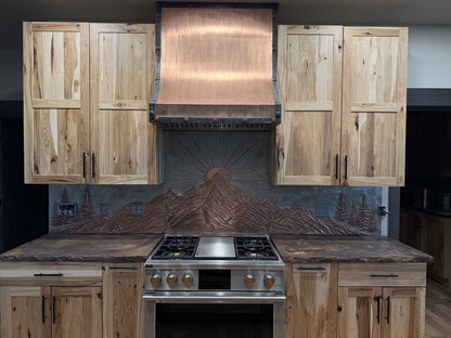 Close-up of hand-hammered copper relief showing mountain sunrise backsplash details