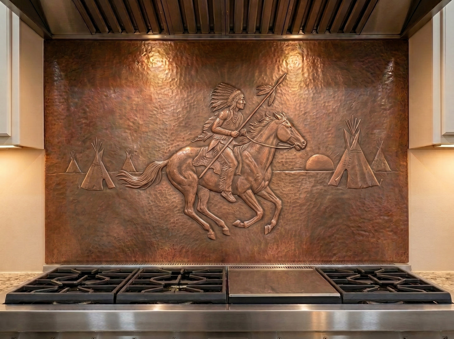 Handcrafted copper stove backsplash installed behind a professional range, featuring a Native American rider on horseback holding a spear in raised relief, with a feather headdress, tipis, setting sun, and hand-hammered copper background in a Western kitchen.