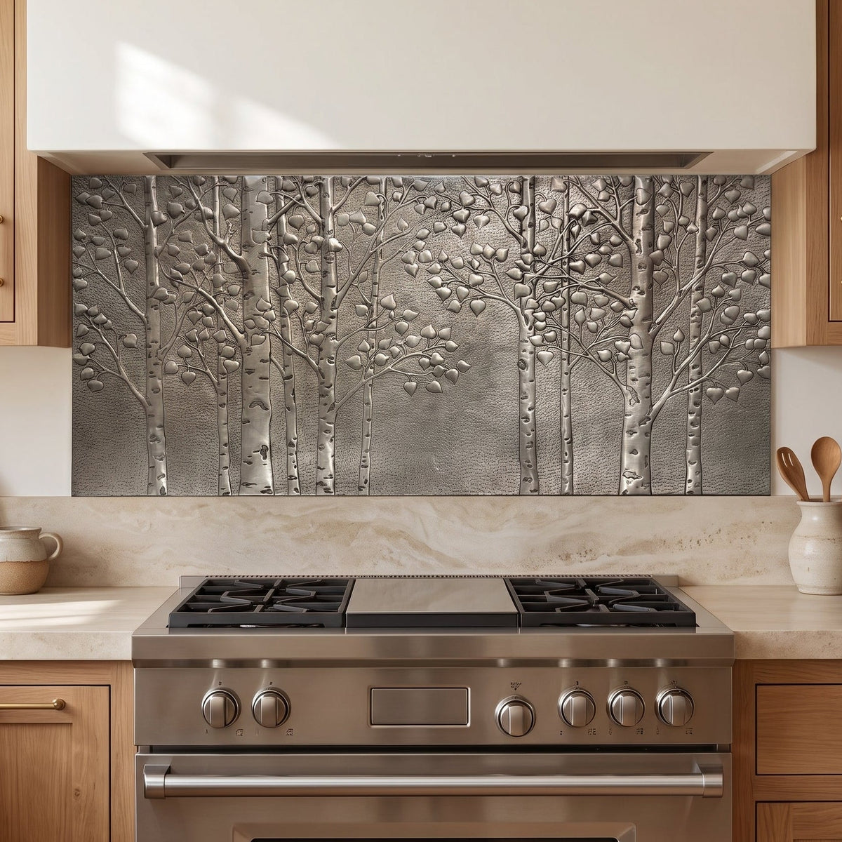 A textured metallic wall backsplash featuring a raised relief design of birch trees, installed in a modern kitchen above a stainless steel gas range.