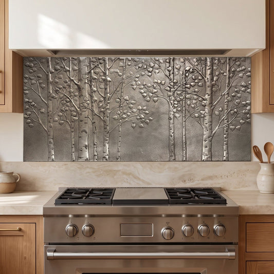 A textured metallic wall backsplash featuring a raised relief design of birch trees, installed in a modern kitchen above a stainless steel gas range.