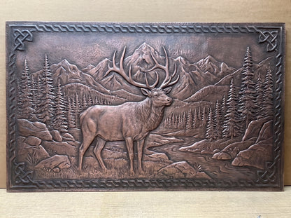 Rocky Mountain Elk handcrafted copper panel featuring a bull elk with large detailed antlers standing in a mountain landscape with pine forests, rocky terrain, distant peaks, and a winding stream, surrounded by a raised Celtic-inspired decorative border.