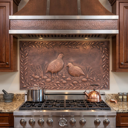 A copper kitchen backsplash tile featuring embossed birds and foliage, installed behind a stainless steel gas range in a wood cabinetry kitchen.