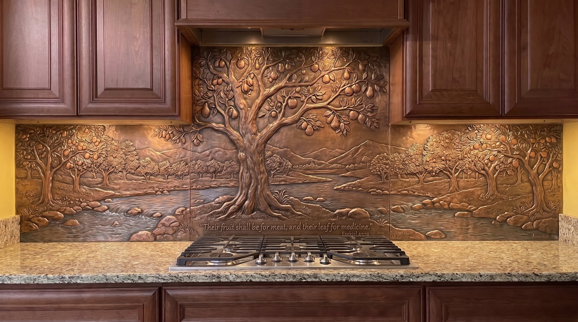 Handcrafted Tree Beside the Waters copper kitchen backsplash inspired by Ezekiel 47:12, with a large fruit-bearing tree beside flowing water and a natural landscape extending across the range wall and under-cabinet copper panels.