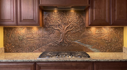 Handcrafted Tree of Life in Eden copper kitchen backsplash inspired by Genesis 2:9, featuring a large Tree of Life in a lush Garden of Eden landscape with dense vegetation, smaller trees, rolling ground, and a stream extending across the copper backsplash behind the range and under the cabinets.