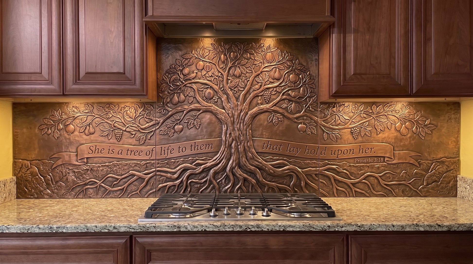 Handcrafted Tree of Life with Deep Roots copper kitchen backsplash inspired by Proverbs 3:18, featuring a large Tree of Life with spreading branches and exposed roots formed in raised relief across the stove backsplash and coordinating under-cabinet panels.
