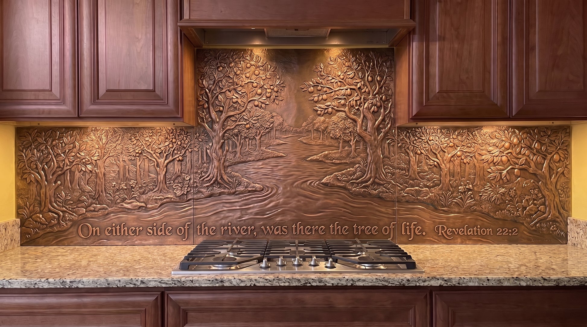 Two Banks of the River of Life copper kitchen backsplash inspired by Revelation 22:2, with a flowing river forming the center of the biblical landscape and abundant trees and foliage along both banks across the stove and under-cabinet backsplash panels.