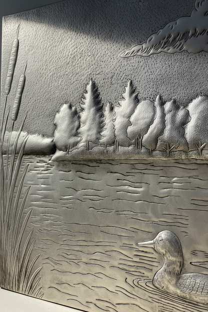 Close-up detail of handcrafted silver lake scene showing raised relief ducks forest and hand-hammered metalwork texture