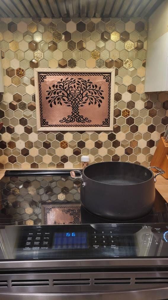 Stovetop with a pot on a hexagonal tiled backsplash featuring a tree of life copper backsplash.