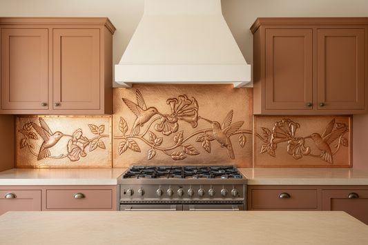 Three copper panels spanning full kitchen wall behind 36-inch range — two hummingbirds in flight with trumpet vine flowers and leaves in repoussé relief on center panel, single hummingbird with vine on each side panel, warm natural copper tone matching magnolia reference, fine stipple background, terracotta shaker cabinets with aged bronze hardware, cream limestone countertop, Mediterranean kitchen
